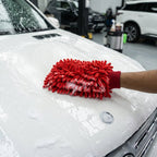 A person's hand in a red microfiber chenille wash glove covered in suds, cleaning the white hood of a car.