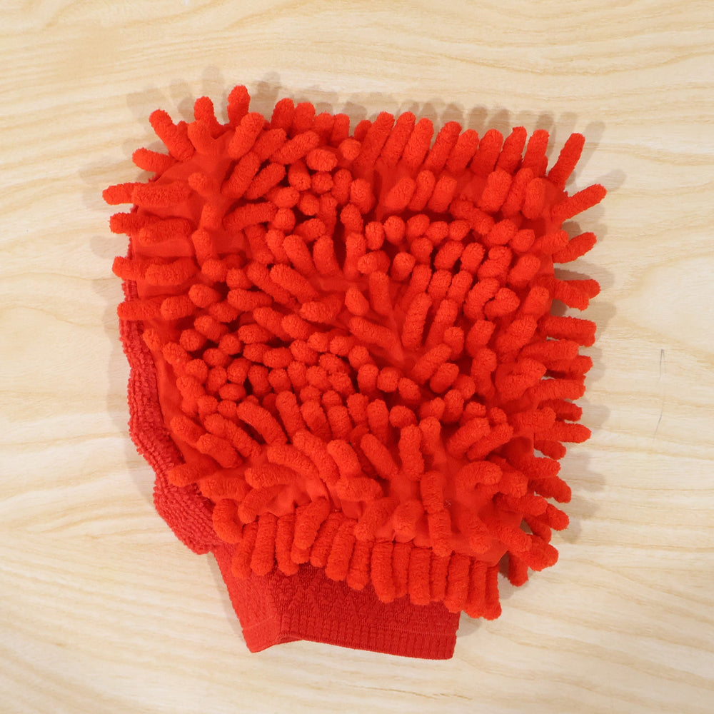 A red microfiber chenille wash glove, with a textured surface, rests on a light wooden surface.