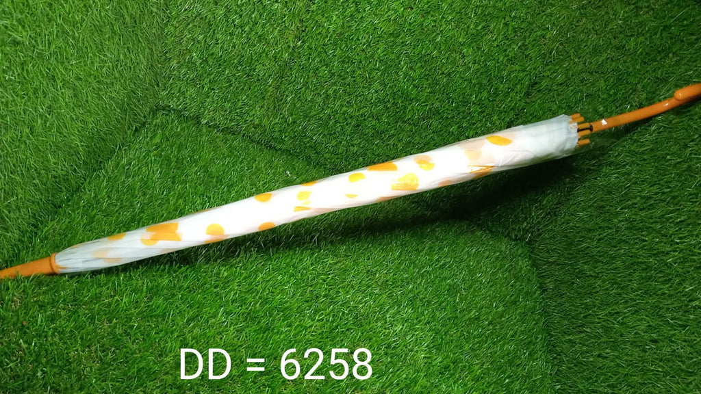 A closed white umbrella with yellow polka dots and a brown handle rests on a vibrant green artificial grass surface.