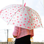 A person from behind holds an open white umbrella with pink polka dots, casting a shadow on a yellow wall.