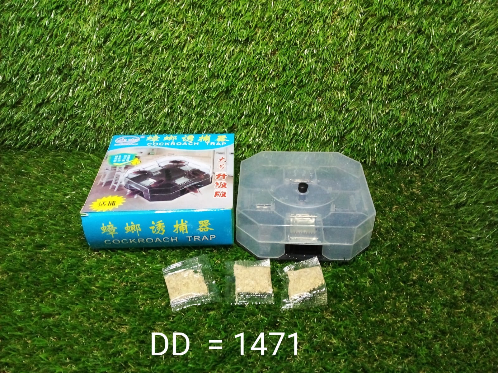 A blue box labeled "COCKROACH TRAP," a clear plastic trap, and three packets of bait are on a green artificial grass surface.