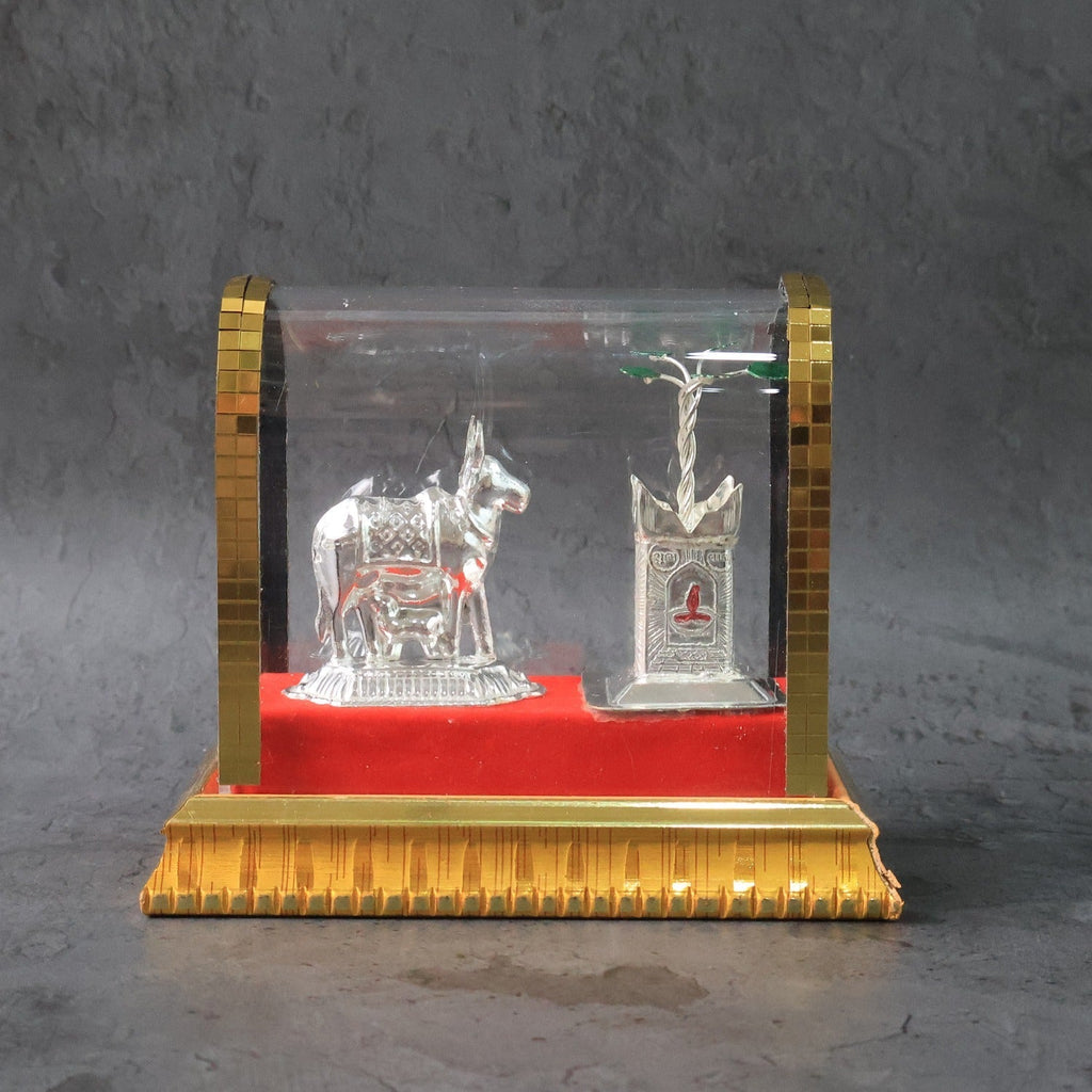 Silver-plated Kamdhenu cow idol set displayed in acrylic case with Tulsi plant