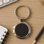 Round metal keychain with black center and chrome finish on white background.